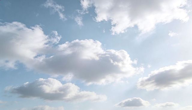 Sunlit cumulus clouds drifting across soft blue sky, serene daylight with streaming rays