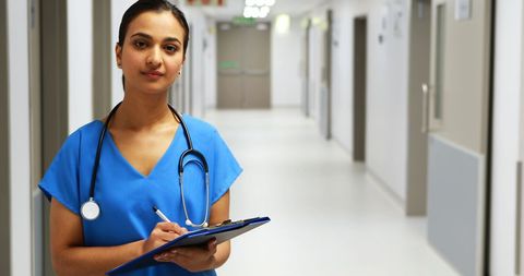 Confident female doctor holding clipboard in hospital corridor