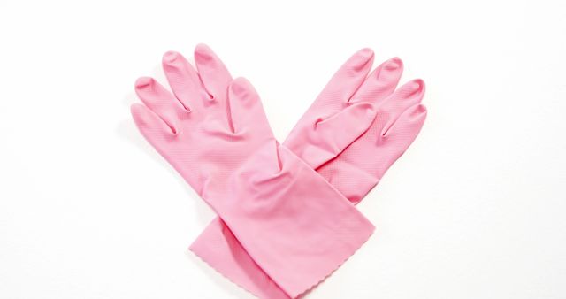 A pair of pink rubber gloves is laid out on a white background, with copy space. These gloves are commonly used for household cleaning and protection against chemicals.