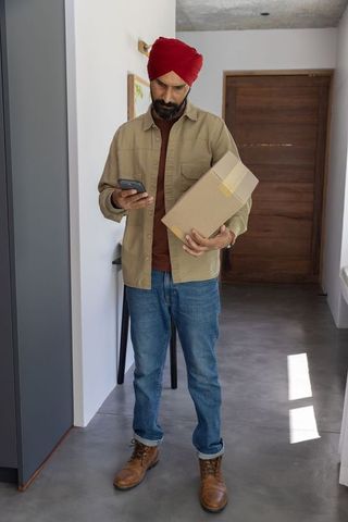 Man in casual attire checking smartphone while holding package