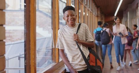 Smiling teen boy at school hallway with backpack ready for class