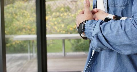 Diverse couple wearing smartwatches and denim standing by sliding door showing intimacy