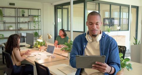African American man holding tablet and wearing headphones in modern open-plan office