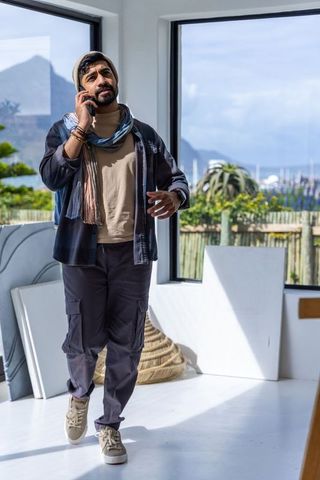 Bearded man walking in sunlit coastal studio talking on phone casual creative lifestyle
