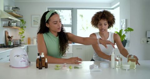 African american women arranging skincare tools and testing led mask on kitchen island