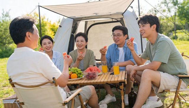 Multi-generation family sharing summer picnic by canvas tent enjoying watermelon and juice