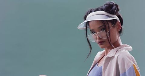 Trendy Woman in Visor and Windbreaker Against Green Background