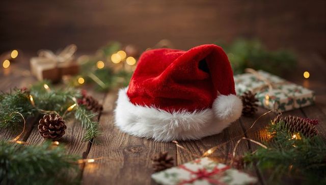 Santa hat resting on rustic wooden table with pinecones, lights and wrapped gifts, cozy still life