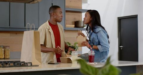 Young Couple Eating Takeout with Chopsticks in Modern Kitchen