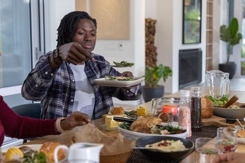 African american man serving salad at family dinner table in modern home