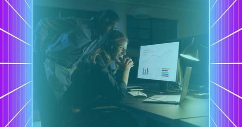 Coworkers collaborating late night analyzing data charts on desktop and laptop, neon teal