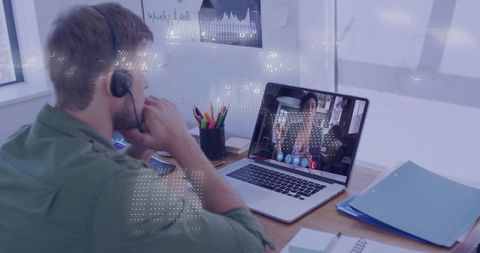 Remote worker wearing headset watching video call with colleague on laptop at desk