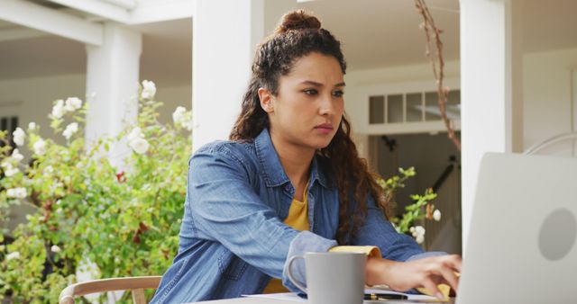 Image of biracial woman using laptop in the garden. Domestic lifestyle and leisure time at home.