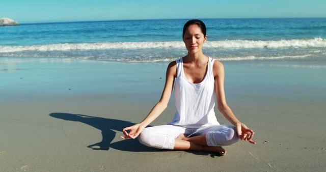 Woman practicing meditation on a serene beach with gentle ocean waves. Ideal for use in mindfulness, wellness, fitness, and lifestyle publications.