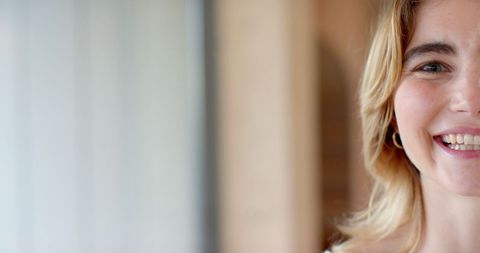 Woman Smiling Indoors with Gold Hoop Earring Near Window Light