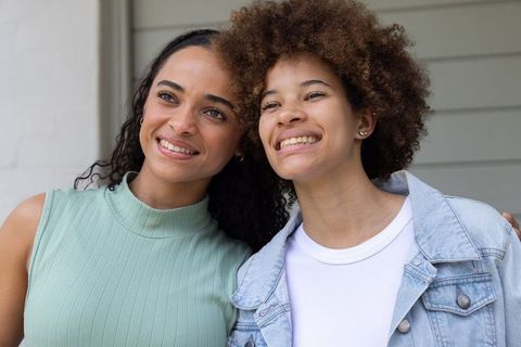 Two african american women smiling on porch wearing denim jacket and pale-green top