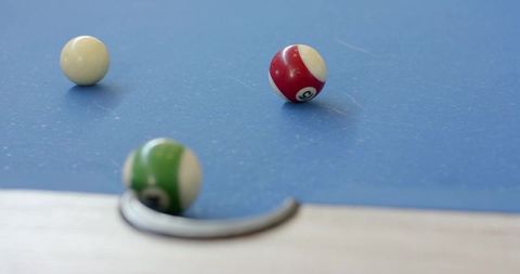 Billiard balls resting on blue felt near pocket rim with shallow depth of field
