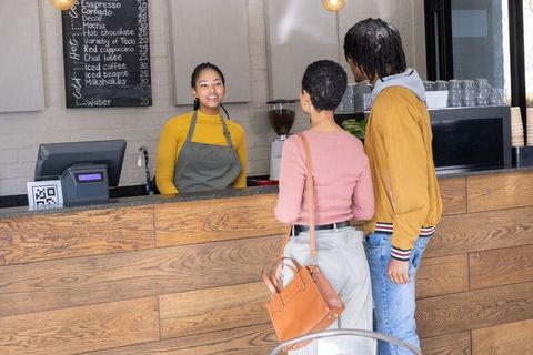Young couple ordering coffee at wooden counter from asian barista using qr code in modern cozy cafe