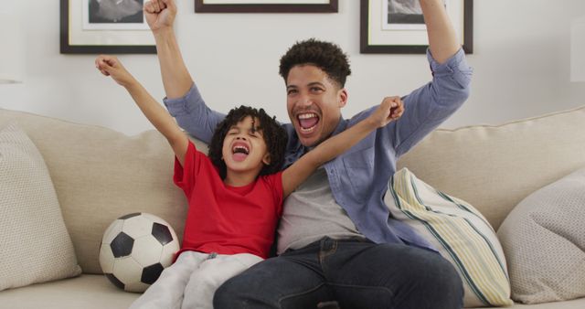 Happy biracial man and his son watching football match together. domestic life, spending time at home.