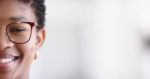 Closeup smiling woman wearing burgundy glasses and gold hoop earring, soft light portrait