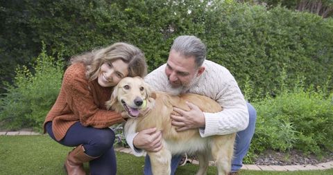 Couple embracing golden retriever in lush backyard