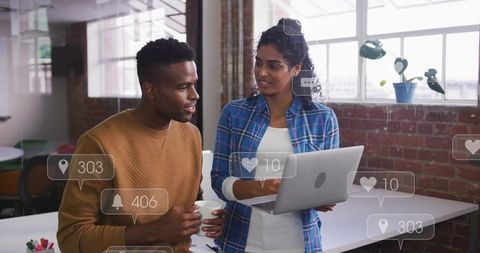 Woman pointing at laptop while colleague holding mug collaborating in bright modern office