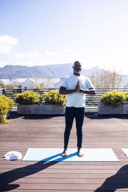 Vertical image of happy african american man practicing yoga in garden. Lifestyle, sport, spending free time at home and garden concept.