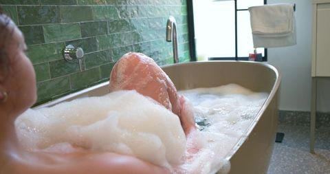 African american woman soaking in freestanding bathtub with bubbles and green tile