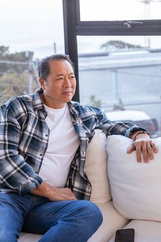 Contemplative Mature Asian Man Relaxing on Sofa at Home