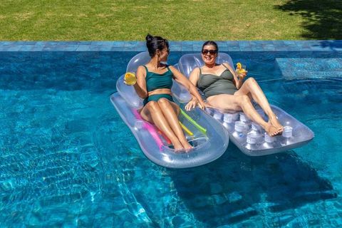Women relaxing on inflatable loungers in backyard pool holding drinks and smiling