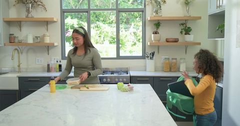 Mother and child preparing school lunches on marble kitchen island in bright modern kitchen