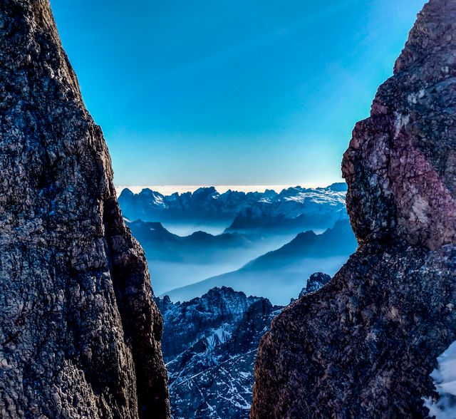Rugged mountain peaks seen through rocky crevice at dawn, with misty layers adding depth to the horizon. Ideal for use in adventure and travel brochures, nature documentaries, posters for outdoor enthusiasts, and inspirational backgrounds.