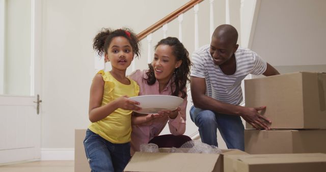 Family joyfully unpacking boxes in their new home, reflecting excitement and fresh beginnings. Daughter helping parents while they bond over the moving process. Ideal for content on family life, moving tips, relocation services, and home renovations.