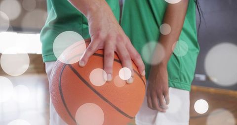 Two Teammates Holding Basketball on Gym Court with Bright Lights