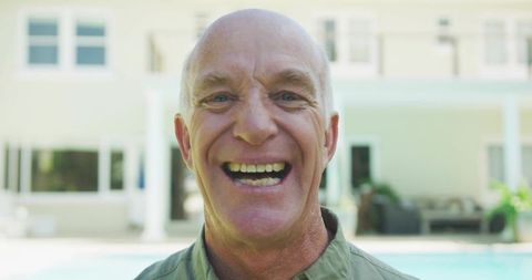 Joyful bald senior man smiling poolside by two-story home retirement lifestyle portrait