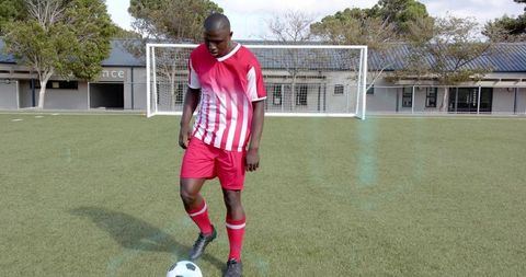 Young male soccer player dribbling ball on school turf near goal during training