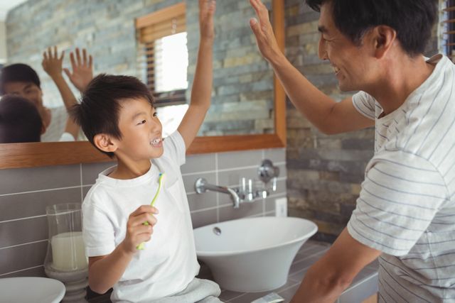 Father and son sharing a joyful moment while brushing teeth in the bathroom. Perfect for themes related to family bonding, morning routines, parenting, and hygiene. Ideal for use in advertisements, blogs, and articles about family life, dental care, and positive parenting.
