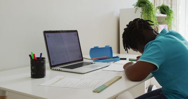 African american boy doing homework looking at laptop with copy space at home. distant education and online class concept