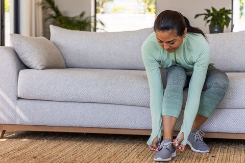Asian woman tying sneakers on sofa preparing for home workout in mint activewear