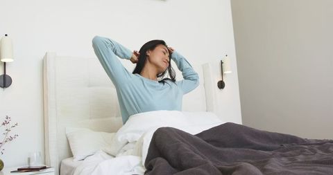 Morning stretch ritual with mid-adult asian woman waking in minimalist modern bedroom