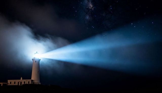 Lighthouse casting twin blue beams across starry night coastal sky with milky way and mist