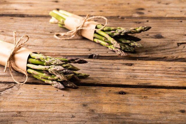 Fresh organic asparagus bunches tied with twine on rustic wooden table. Ideal for use in food blogs, healthy eating promotions, farm-to-table concepts, and seasonal vegetable features. Perfect for illustrating recipes, nutrition articles, and vegan or vegetarian lifestyle content.