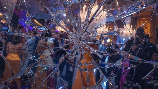 Shattered mirror starburst revealing glamorous ballroom with chandeliers and guests