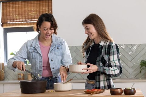 African american woman and friend cooking together in bright kitchen, sharing meal prep