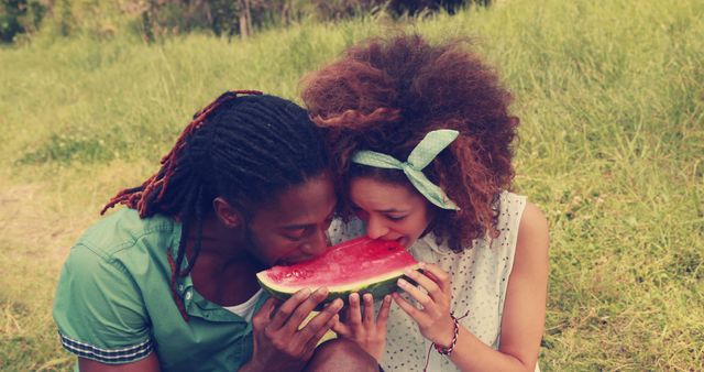 A young African American man and a biracial girl are sharing a slice of watermelon outdoors, with copy space. Their joyful interaction while enjoying a summer treat captures a moment of simple pleasure and connection.