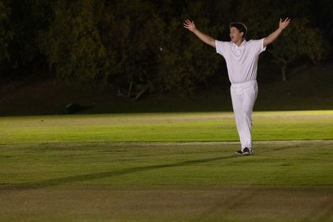 Night cricket player celebrating appeal under floodlights on open grass field
