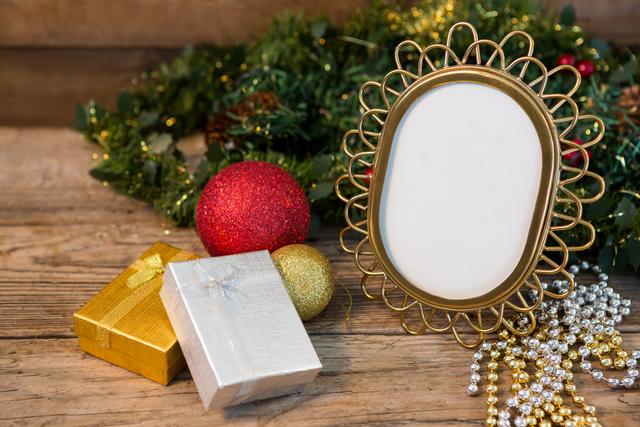 This image features Christmas decorations including a garland, baubles, and an empty frame on a wooden table. Ideal for holiday greeting cards, festive invitations, seasonal blog posts, and social media content.