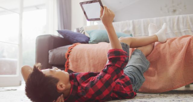 Boy lying on floor in casual clothing using tablet at home. Ideal for use in articles about kids and technology, home lifestyles, indoor activities, and modern parenting.