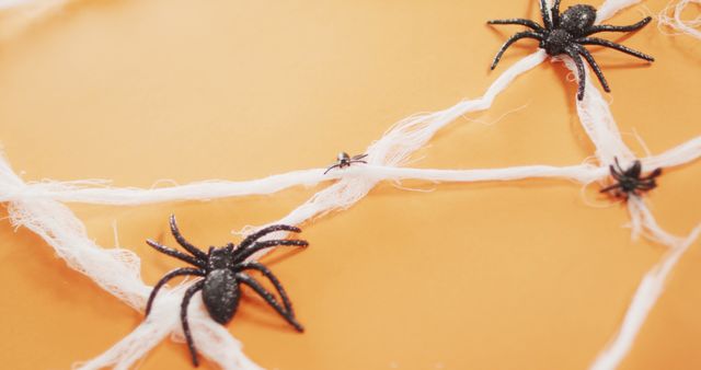 Close up of multiple spider toys forming a spider web against orange background. halloween festivity and celebration concept
