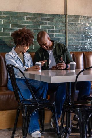 African american couple laughing while looking at smartphone in cozy cafe